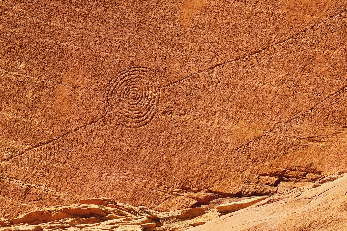 Petroglyph of concentric circles carved into a reddish sandstone wall.