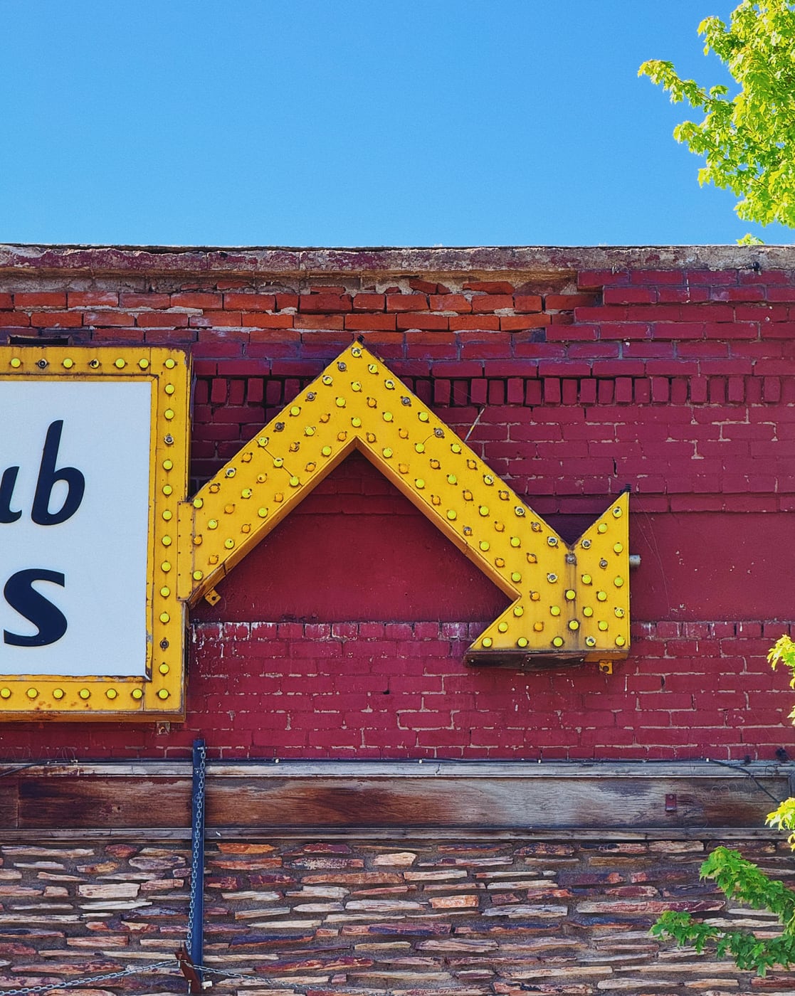 Vintage yellow arrow sign with lights on a red brick building against a clear blue sky with stacked stone masonry on the building below the brick.