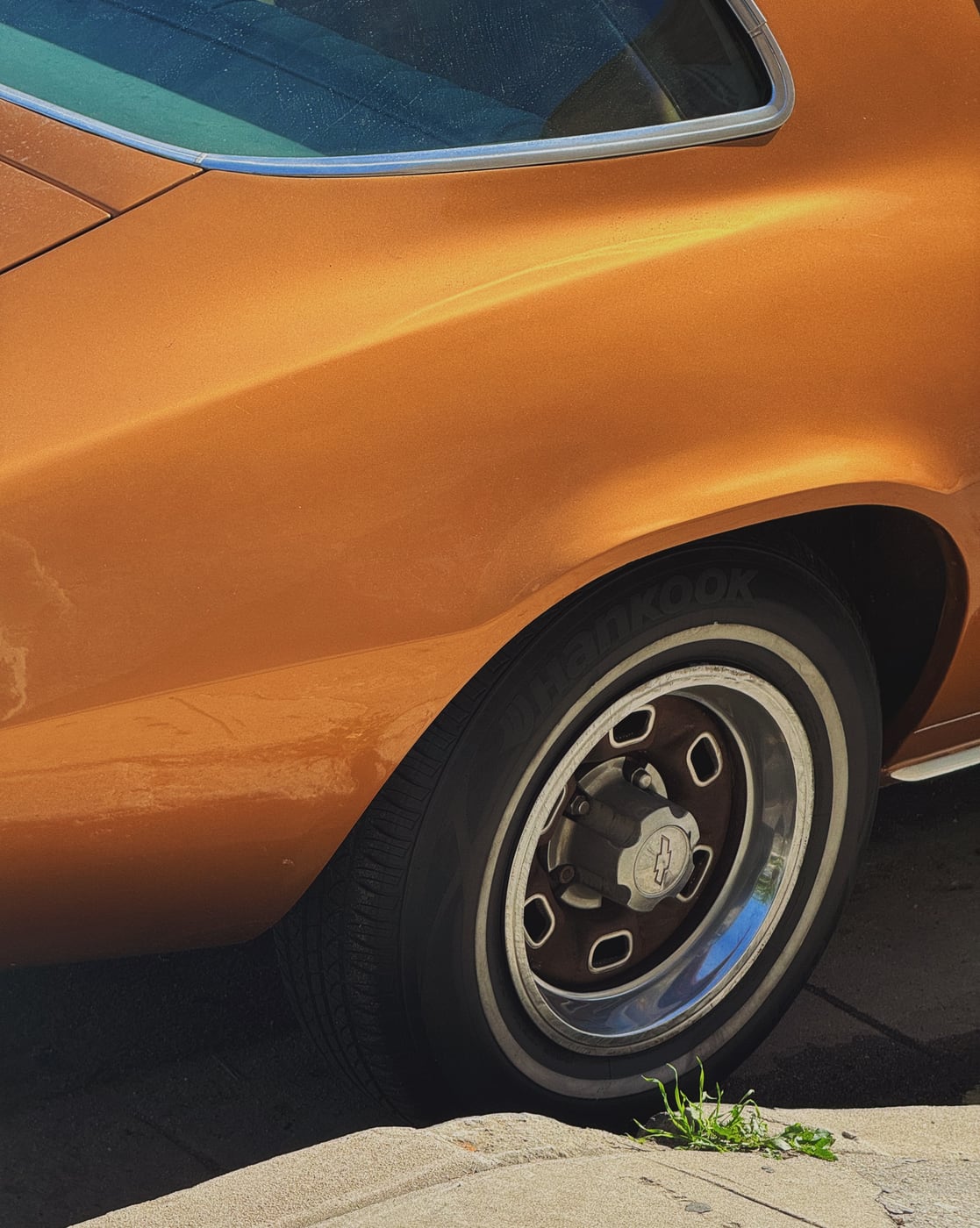 Close-up of the rear wheel and curved side panel of a classic car with a metallic, copper-colored paint job.