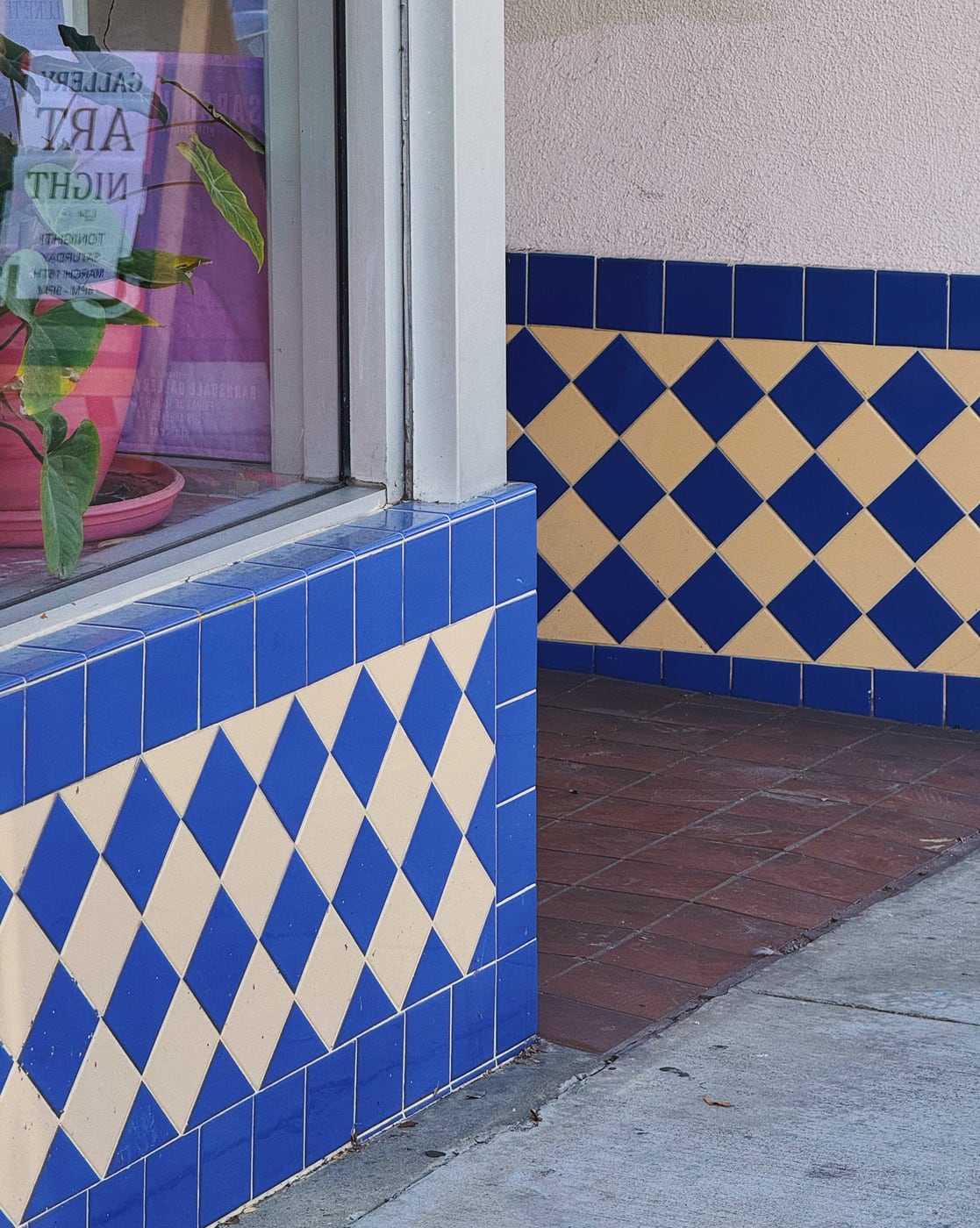 Exterior corner of a retail storefront entrance with blue and cream diamond-patterned tiles near a sidewalk.